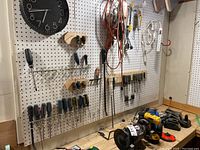 Wide view of workshop pegboard with screwdrivers, trouble lamps, power tools, grinder and cords on workbench