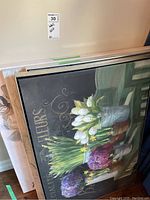 Four stacked unframed canvas floral wall art pieces leaning against wall, visible flower art and size indication