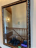 Full view of the large rectangular wall mirror with a beveled edge and ornate dark frame featuring floral and leaf carving patterns.