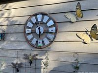 Photo of the entire wall display showing clock, metal butterflies, and insect ornaments outside on siding.