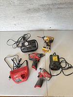 Overall view of power tools and chargers on table showing Milwaukee and DeWalt brands and assorted power tools and accessories.