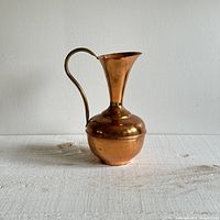 Front view of a copper and brass large pitcher showing the bulbous copper body with a flared top and brass curved handle.