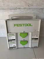 Front view of two lidded Festool plastic stacking organizer cases with green latches and Festool logo.