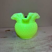 Close-up photo showing the vase glowing bright green under UV light, highlighting the uranium milk glass property.