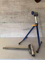 Full view of the folding roller stand showing blue tripod legs and height adjustable roller.