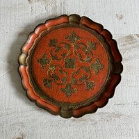 Top view of the round scalloped edge orange Florentine serving tray with gold embossed floral design in the center on a white surface.