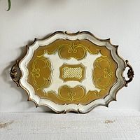 Front view of decorative Italian Florentine tray showing scalloped edges and embossed abstract gold design on white background with ornate handles.