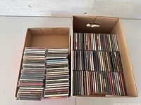 Two boxes filled with stacked music CDs in jewel cases lined up and neatly arranged