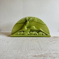 Front view of a glossy light green ceramic deer vase holder with arched back and detailed rock base.