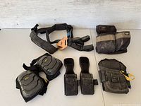 Photo shows a collection of black construction tool pouches, a padded adjustable harness with 'Kims' leather patch, and black cushioned knee pads.