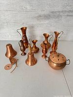 Overview of all copper items in lot showing different sizes and types including pitchers, bells, pot and strainer.
