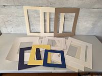Overview of assorted frame mattes of various colors and sizes laid out on a table, showing a mix of white, navy blue, yellow, cream, and taupe mattes.