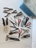 Multiple pliers and snips laid out next to a blue plastic storage tote, showing size and condition variety