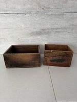 Front view of two vintage wooden crates side by side on a light surface against a weathered wooden background.