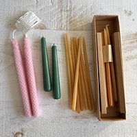 Three groups of wax taper candles arranged on a white surface: pink spiral patterned pair, two green candles, and eleven natural beeswax candles with some boxed.