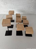 Ten small wooden blocks on black metal stands arranged on a table surface, showing variation in height and size.