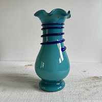 Front view of vintage blue art glass vase with ruffled edge and dark blue swirl detailing on neck, placed on a flat surface with white background.