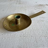 Photo showing vintage brass candle holder with flat long handle, circular base, and some aging/tarnish.