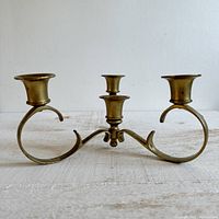 Front angled view of vintage brass four-cup candelabra with curved base and ornate detailing.