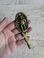 Close-up photo showing the full brass wall hook with Tony Weller character relief held in hand for scale.