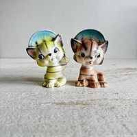 Front view of both vintage cat salt and pepper shakers wearing bonnets placed on a textured surface.