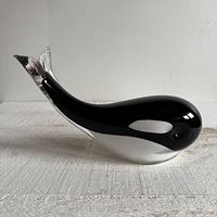Side view of the black, white, and clear glass whale sculpture on a white textured surface.