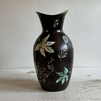 Front view of the vase showing foliage designs on the dark matte ceramic surface, flared rim and yellow interior.