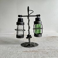 Front view of the vintage nautical glass hanging lantern salt and pepper shakers on a metal anchor stand, showing the clear and green glass shakers suspended from the metal stand.