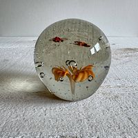 Front view of glass paperweight showing the orange flower and bugs inside with air bubbles.