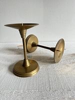 Side angle view of one brass votive candle holder standing and one lying down showing details of spike and stepped design