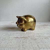 Side view of the brass piggy bank showing its detailed pig shape and overall condition with minor surface wear.