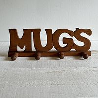 Front view of wooden MUGS peg rack for hanging mugs, showing the letters and four pegs.