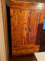 Front view of a two-door custom hardwood cabinet with visible wood grain and rustic metal hinges and lock.