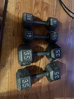 Four hex dumbbells on wooden floor. Two 35 lb dumbbells and two 15 lb dumbbells, arranged side by side.