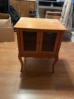 Front view of wooden end table with glass doors showing the overall shape, curved legs, and glass panels.