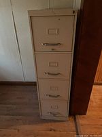 Front view of tall beige 4-drawer metal filing cabinet showing handles and label holders.
