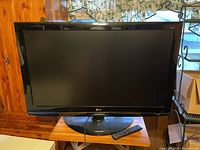 Front view of the LG flat-screen TV showing the full screen and base stand with remote lying in front.