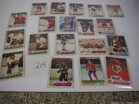 Layout of 20 vintage 1977 NHL hockey cards on carpet, with a paper numbered 215 included for lot identification.