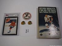 Photo showing a 1970 Stan Mikita autobiography book, two Chicago Blackhawks crest patches, and the graded Stan Mikita hockey card.