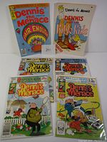 Four Dennis The Menace comic books displayed together in protective sleeves, arranged in two rows of two. Covers are colorful with various cartoon illustrations of Dennis The Menace. Issues numbered 1, 2, 3, and 4 are visible.