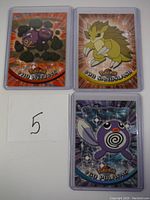 Three holographic 2000 Topps Pokemon cards featuring Weezing, Sandslash, and Poliwag, arranged with a handwritten number 5.