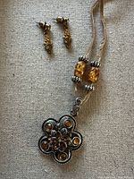 Full view of matching beaded necklace with flower pendant and small dangling earrings on beige fabric background.