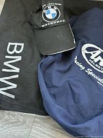 Full view of black BMW bag, black BMW logo baseball cap, and blue Arai helmet bag.