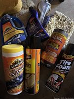 Photo showing front view of various car cleaning products including Armor All Car Wash soap, Armor All Tech Wax 2.0, Armor All Air Fresh Cleaner wipes, Tri D-Tex Ultimate Leather Care, and Meguiar's Tire Foam with applicators.