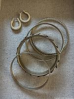 Full view of gold-tone textured hoop earrings with four gold-tone bracelets, including a black and gold woven cuff, on fabric background.