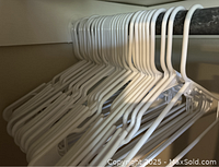 25 white plastic hangers hanging on a closet rod shown in lines, all of same style and design.