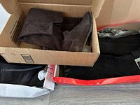 Dark brown suede boot with fold-over cuff inside a cardboard box, showing gently used condition.