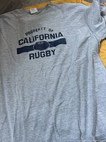 Gray short sleeve Cal Rugby T-shirt with navy blue screen print "Property of California Rugby" and a rugby ball graphic.