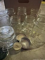 Overall view of miscellaneous mason jars and canning jars with some lids and metal clamp lid in foreground.