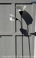 Full view of the black dual-arm floor lamp with two white glass lampshades against grey wall.